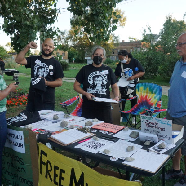 A group of activists wearing masks and black t shirts stand behind a table covered with literature about freeing political prisoners