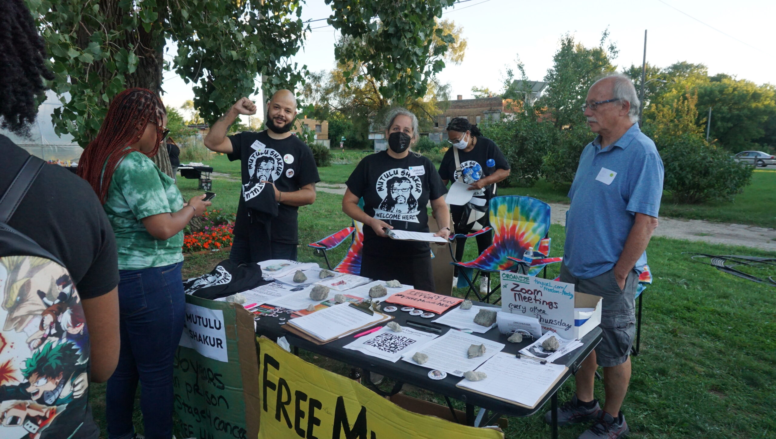 A group of activists wearing masks and black t shirts stand behind a table covered with literature about freeing political prisoners