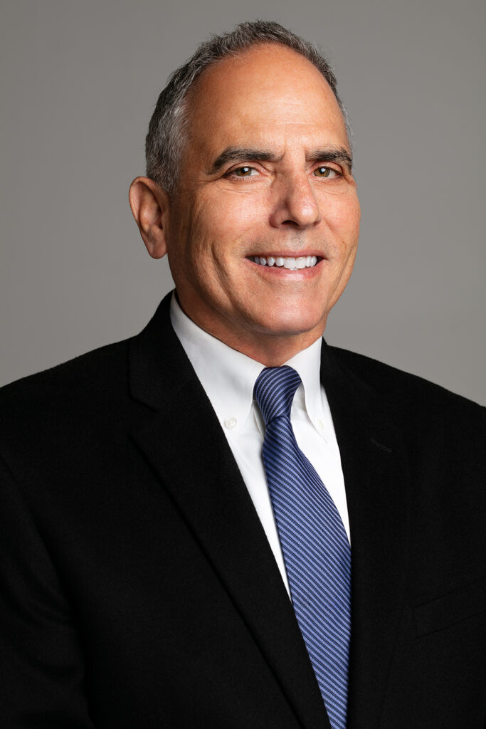 A headshot of our staff attorney, Mark J. Bennett in a black suit and blue striped tie